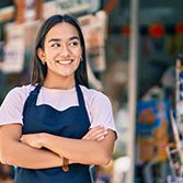 Young latin shopkeeper girl with arms crossed smiling happy at the press shop